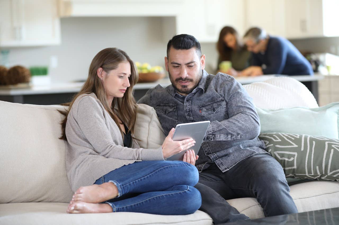 Hispanic man and woman sitting on couch with tablet.
