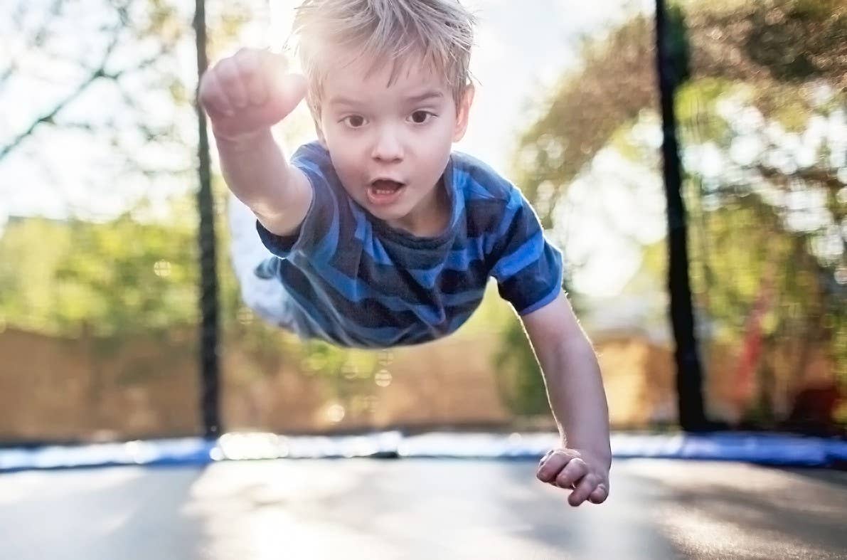 Boy strikes super hero pose on trampoline